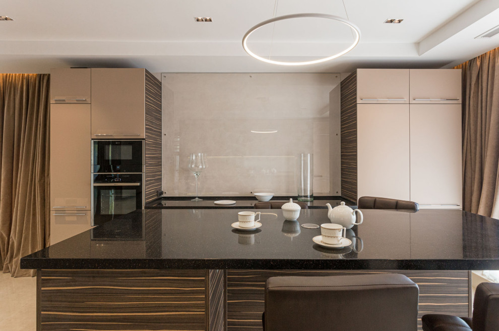 Photo of an expansive contemporary galley kitchen/diner in Saint Petersburg with a single-bowl sink, flat-panel cabinets, beige cabinets, composite countertops, black appliances, porcelain flooring, an island, beige floors, black worktops and a drop ceiling.