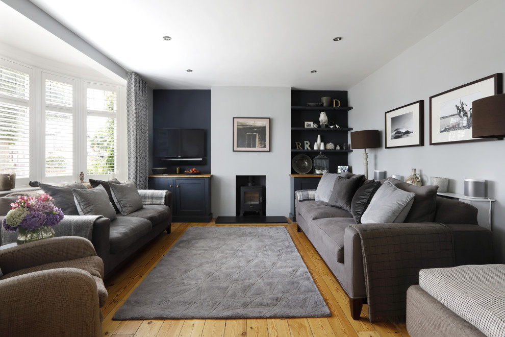 Photo of a mid-sized contemporary living room in Sussex with grey walls, medium hardwood floors, a wood stove, a wall-mounted tv, beige floor and a plaster fireplace surround.