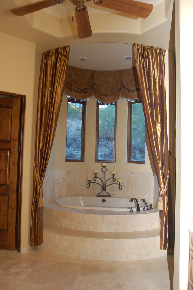 This is an example of a mid-sized mediterranean master bathroom in Phoenix with a drop-in tub, an open shower, a one-piece toilet, beige tile, ceramic tile, beige walls, ceramic floors and a drop-in sink.
