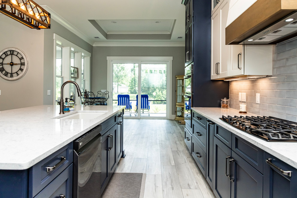 Photo of a large beach style l-shaped eat-in kitchen in Atlanta with a drop-in sink, shaker cabinets, blue cabinets, marble benchtops, glass tile splashback, light hardwood floors, with island, grey floor and multi-coloured benchtop.