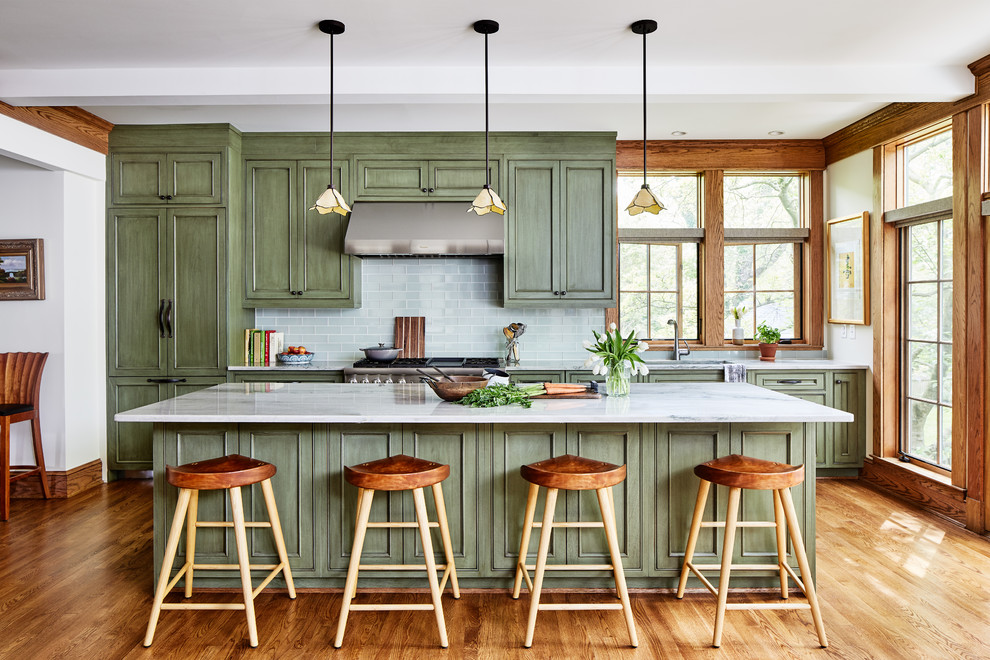 This is an example of a mid-sized arts and crafts single-wall open plan kitchen in DC Metro with an undermount sink, recessed-panel cabinets, green cabinets, quartz benchtops, green splashback, glass tile splashback, panelled appliances, medium hardwood floors, with island, brown floor and grey benchtop.