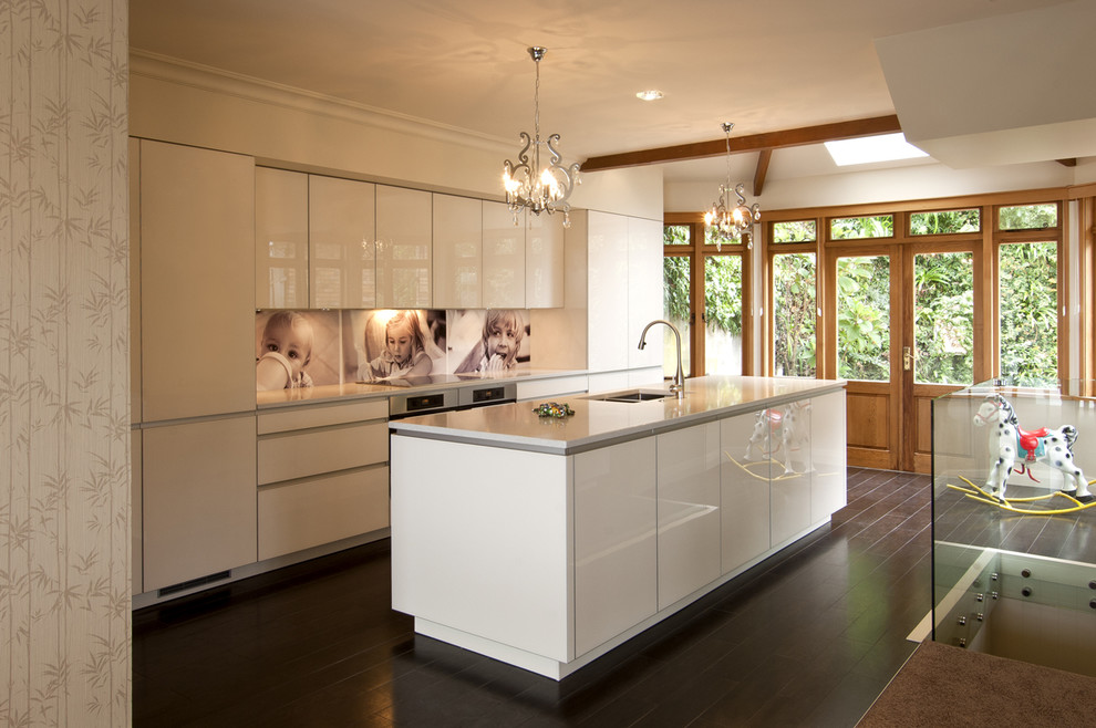 This is an example of a contemporary kitchen in Wellington with an undermount sink, white cabinets, quartz benchtops, multi-coloured splashback, glass sheet splashback, coloured appliances, dark hardwood floors, with island and flat-panel cabinets.