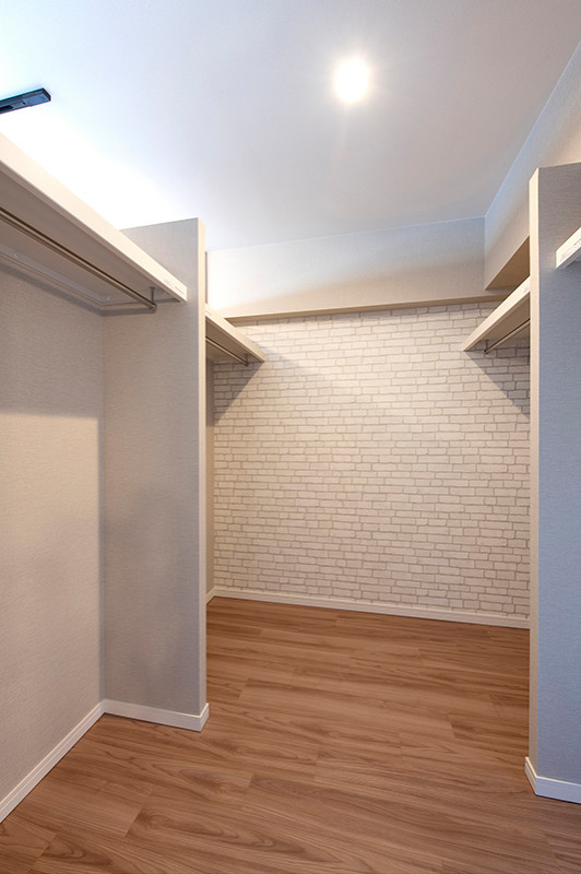 Cette image montre un petit dressing nordique neutre avec un placard sans porte, des portes de placard blanches, un sol en contreplaqué, un sol marron et un plafond en papier peint.