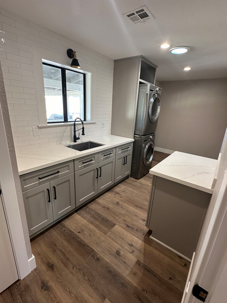 Design ideas for a large arts and crafts galley laundry room in Phoenix with a single-bowl sink, shaker cabinets, grey cabinets, quartz benchtops, white splashback, ceramic splashback, green walls, laminate floors, a stacked washer and dryer and white benchtop.