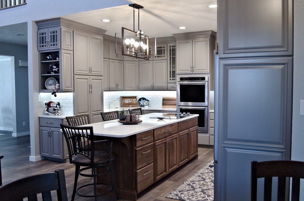 U-shaped brown floor eat-in kitchen photo with a double-bowl sink, raised-panel cabinets, gray cabinets, marble countertops, white backsplash, stainless steel appliances, an island and white countertops