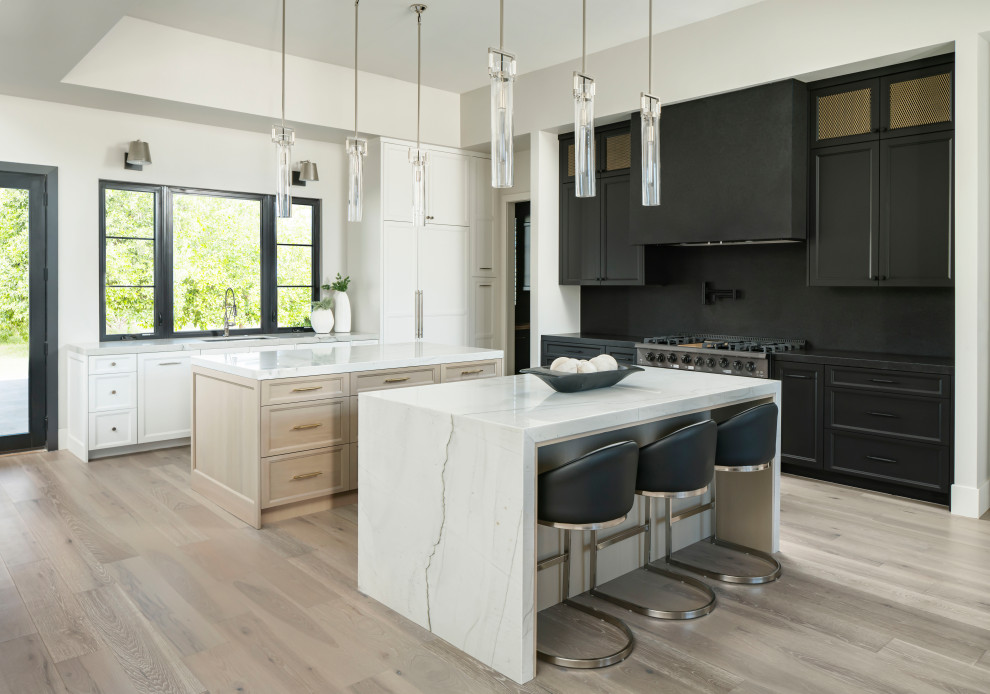 Huge transitional l-shaped light wood floor and gray floor open concept kitchen photo in Phoenix with a double-bowl sink, recessed-panel cabinets, black cabinets, granite countertops, black backsplash, stone slab backsplash, paneled appliances, two islands and black countertops