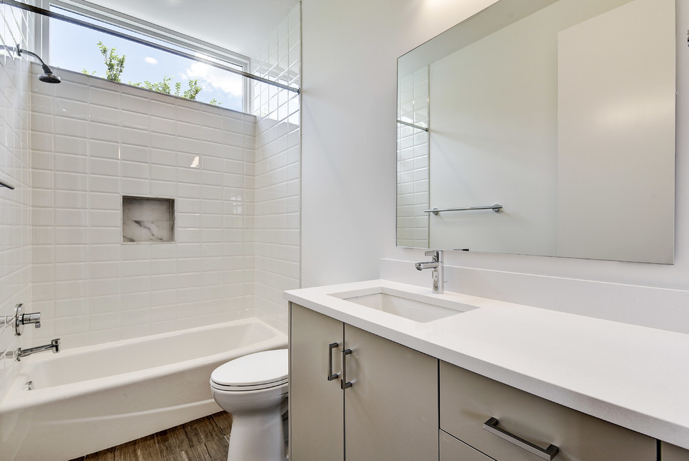 Inspiration for a modern kids bathroom in Austin with flat-panel cabinets, grey cabinets, an alcove tub, a shower/bathtub combo, a two-piece toilet, white tile, porcelain tile, white walls, medium hardwood floors, an undermount sink, engineered quartz benchtops and a shower curtain.
