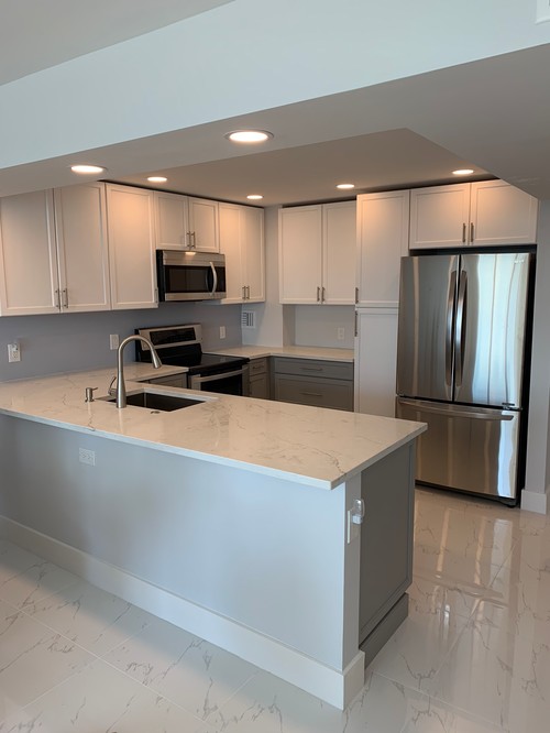 L-shaped condo kitchen with white cabinets, peninsula island, and stainless steel appliances