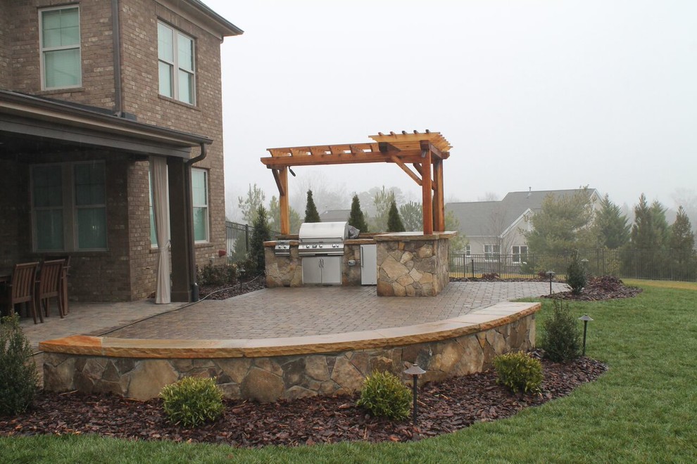 Photo of a large transitional backyard patio in Charlotte with an outdoor kitchen, brick pavers and a pergola.