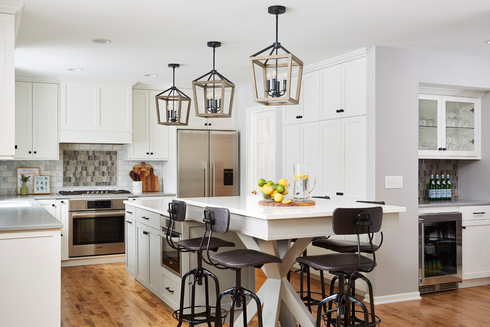 This is an example of a transitional kitchen in Minneapolis with shaker cabinets, white cabinets, multi-coloured splashback, stainless steel appliances, medium hardwood floors, with island and white benchtop.