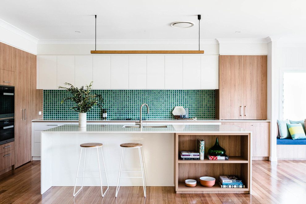 Design ideas for a contemporary l-shaped kitchen in Brisbane with an undermount sink, flat-panel cabinets, white cabinets, green splashback, stainless steel appliances, medium hardwood floors, with island, brown floor and white benchtop.