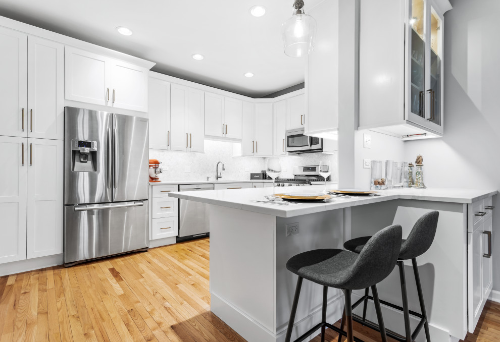 Mid-sized transitional u-shaped medium tone wood floor enclosed kitchen photo in Chicago with an undermount sink, shaker cabinets, white cabinets, quartz countertops, white backsplash, stainless steel appliances, no island and white countertops