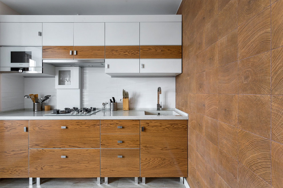 This is an example of a small contemporary single-wall separate kitchen in Moscow with an integrated sink, flat-panel cabinets, medium wood cabinets, quartz benchtops, white splashback, ceramic splashback, white appliances, porcelain floors, grey floor and white benchtop.