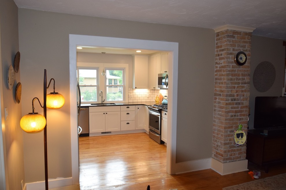 Transitional u-shaped light wood floor kitchen photo with an undermount sink, shaker cabinets, white cabinets, quartz countertops, white backsplash, subway tile backsplash, stainless steel appliances, no island and black countertops