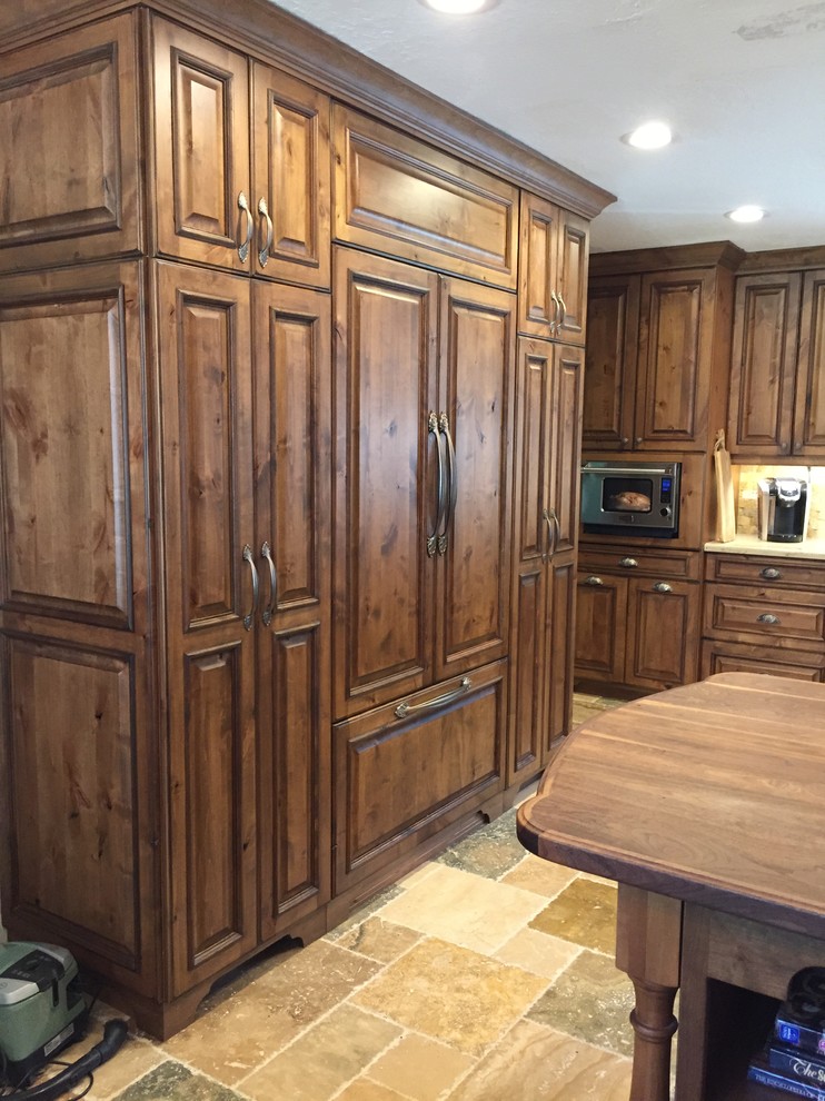 This is an example of a mid-sized traditional l-shaped eat-in kitchen in Houston with a farmhouse sink, raised-panel cabinets, limestone benchtops, beige splashback, stone tile splashback, panelled appliances, a peninsula, dark wood cabinets and slate floors.