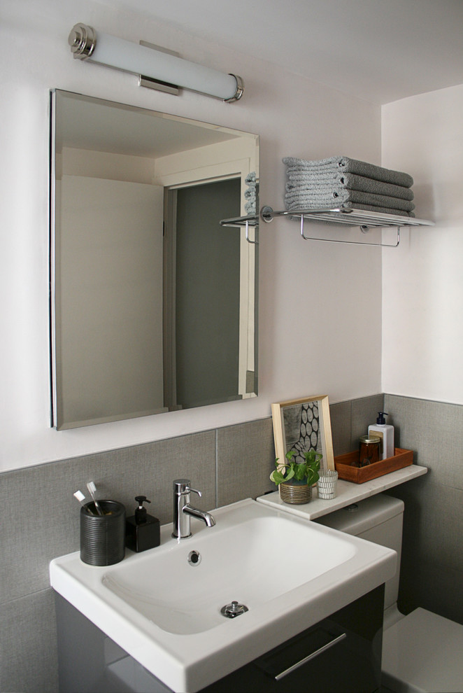 Inspiration for a small scandinavian bathroom in New York with a wall-mount sink, flat-panel cabinets, grey cabinets, marble benchtops, a drop-in tub, a shower/bathtub combo, a two-piece toilet, gray tile, subway tile, white walls and ceramic floors.