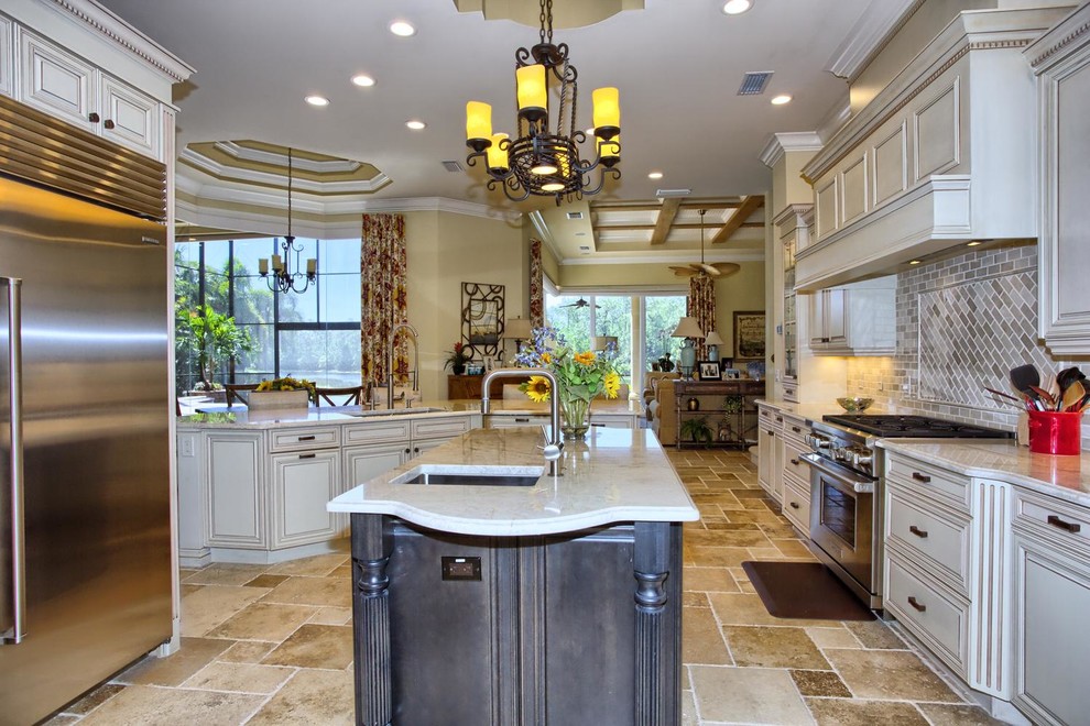 Design ideas for a traditional kitchen in Miami with an undermount sink, raised-panel cabinets, white cabinets, quartzite benchtops, beige splashback, stone tile splashback, stainless steel appliances, travertine floors and multiple islands.