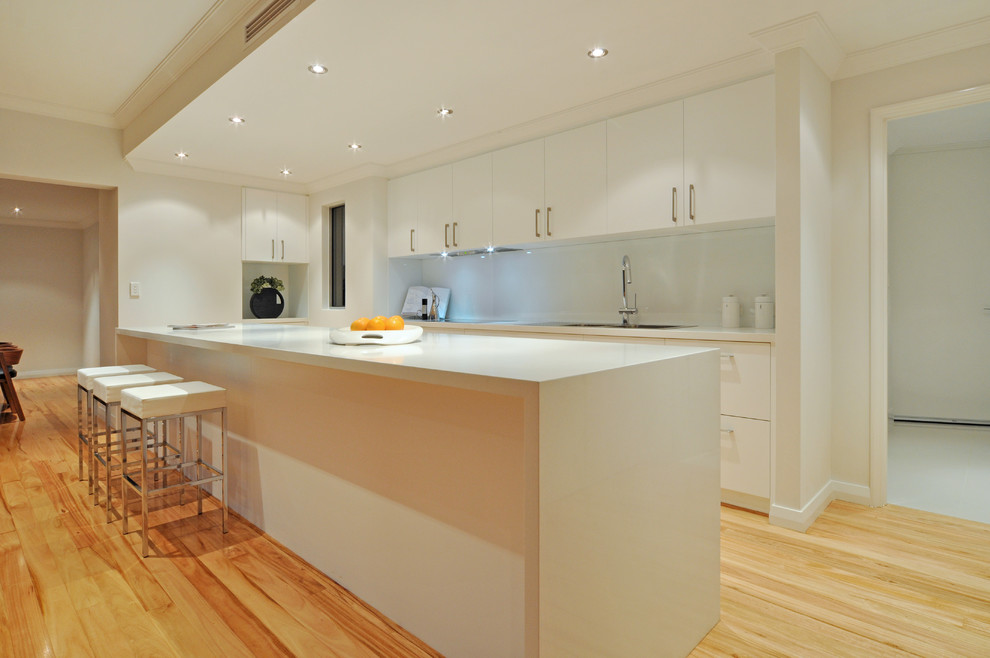 Large contemporary galley eat-in kitchen in Perth with a drop-in sink, flat-panel cabinets, white cabinets, quartz benchtops, white splashback, glass sheet splashback, stainless steel appliances, medium hardwood floors and with island.