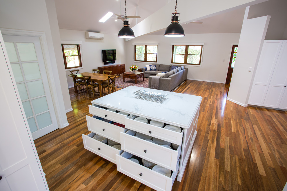 This is an example of a large traditional u-shaped open plan kitchen in Brisbane with a double-bowl sink, shaker cabinets, white cabinets, quartz benchtops, white splashback, subway tile splashback, black appliances, medium hardwood floors, with island and brown floor.