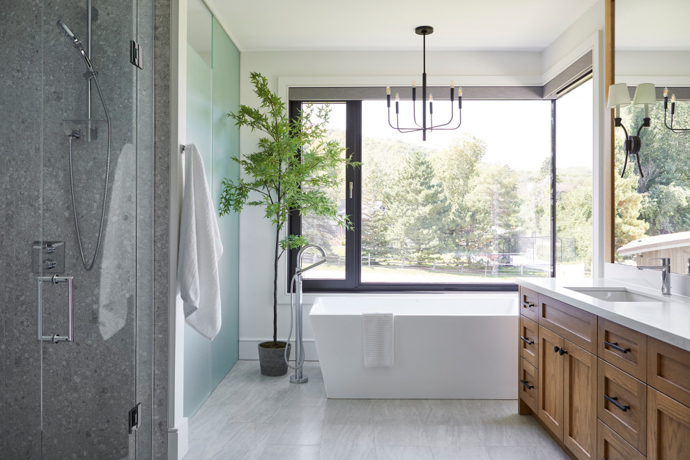 Inspiration for a transitional bathroom in Toronto with shaker cabinets, medium wood cabinets, a freestanding tub, an alcove shower, white walls, an undermount sink, grey floor, a hinged shower door, white benchtops, a double vanity and an enclosed toilet.