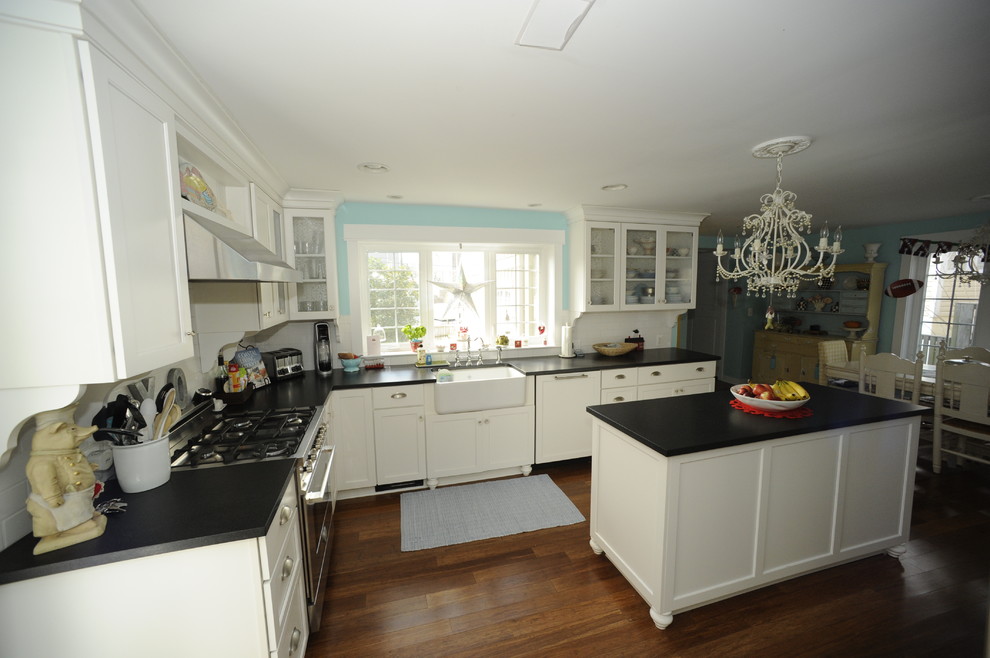 Large transitional u-shaped medium tone wood floor enclosed kitchen photo in Baltimore with a farmhouse sink, glass-front cabinets, white cabinets, soapstone countertops, white backsplash, subway tile backsplash, stainless steel appliances and an island