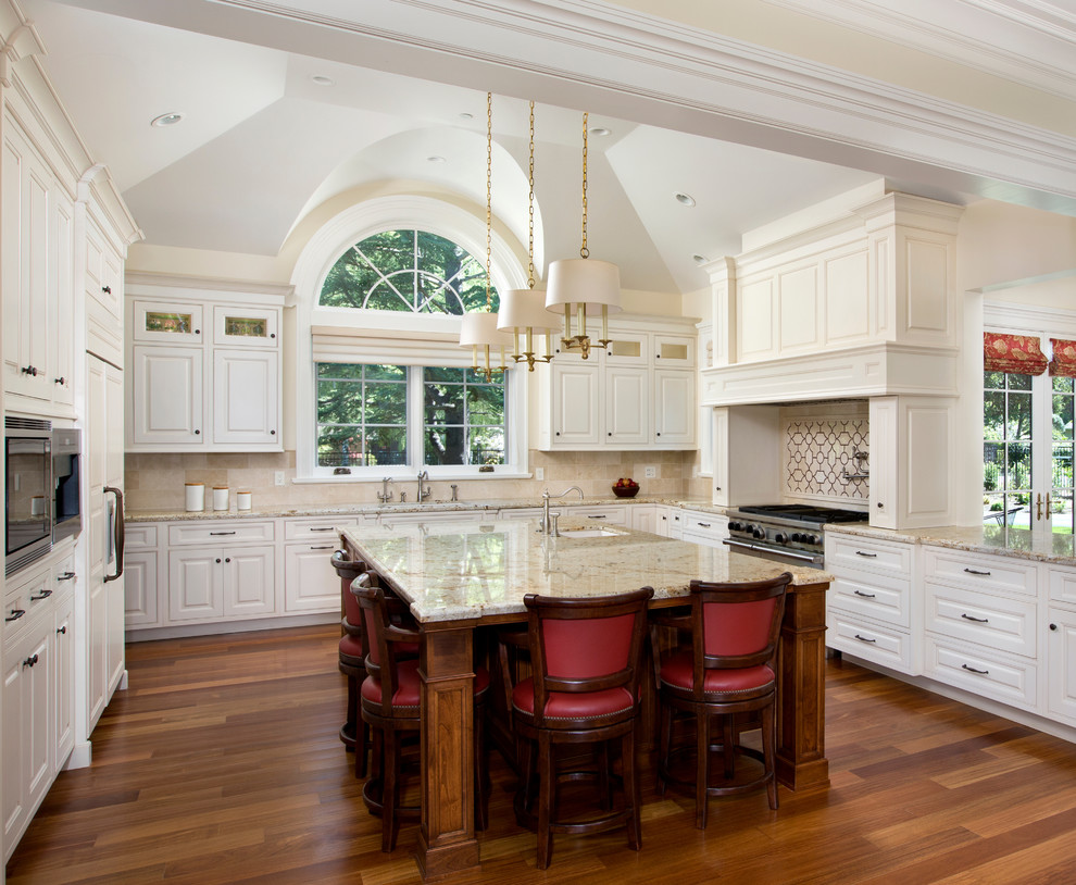 Photo of a large traditional u-shaped kitchen in San Francisco with granite benchtops, raised-panel cabinets, white cabinets, beige splashback, stainless steel appliances, an undermount sink, medium hardwood floors, with island and beige benchtop.