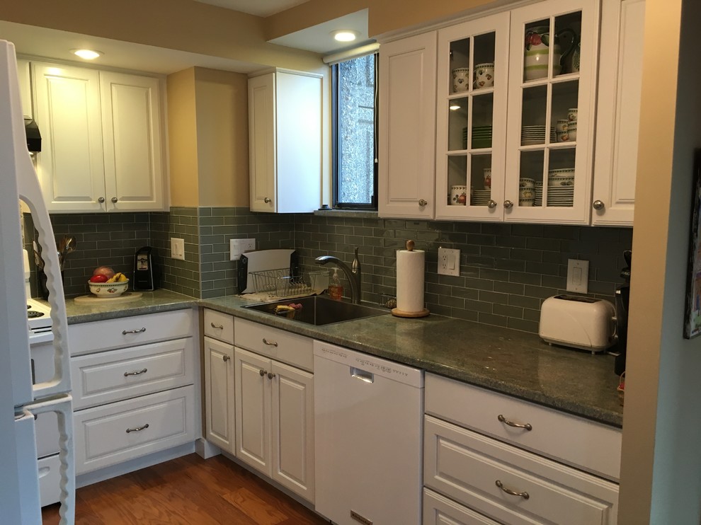 This is an example of a transitional u-shaped kitchen in Boston with a drop-in sink, raised-panel cabinets, white cabinets, granite benchtops, green splashback, glass tile splashback, white appliances, medium hardwood floors, a peninsula and green benchtop.