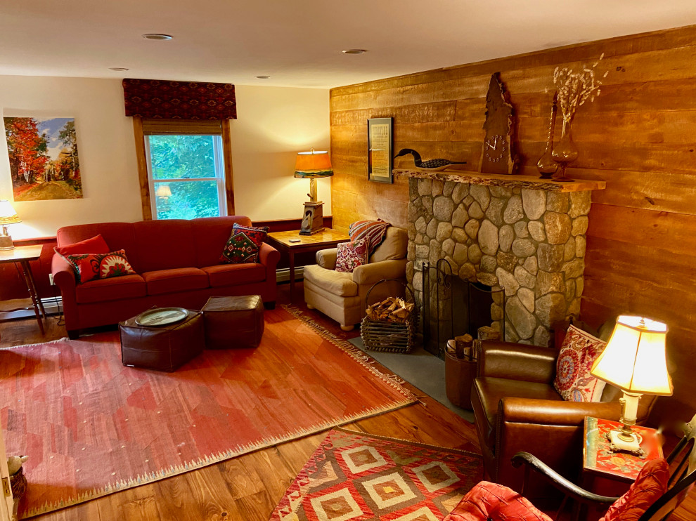 Пример оригинального дизайна: изолированная гостиная комната среднего размера в стиле фьюжн с оранжевыми стенами, паркетным полом среднего тона, стандартным камином, фасадом камина из камня, телевизором на стене, коричневым полом и стенами из вагонки