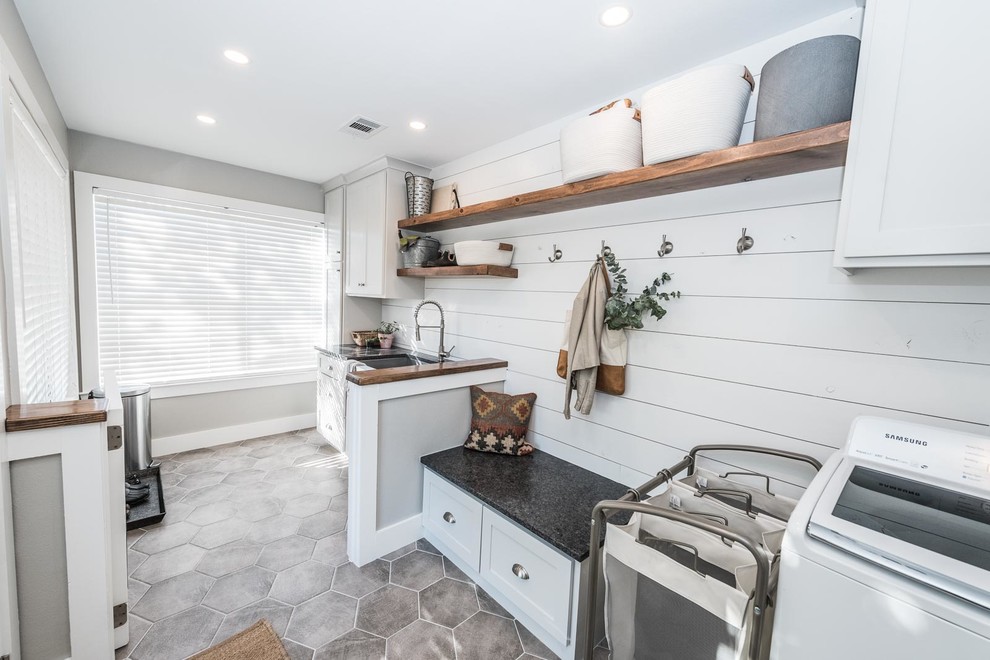 Inspiration for a large country galley dedicated laundry room in Dallas with a farmhouse sink, shaker cabinets, white cabinets, granite benchtops, white walls, ceramic floors, a side-by-side washer and dryer, grey floor and black benchtop.