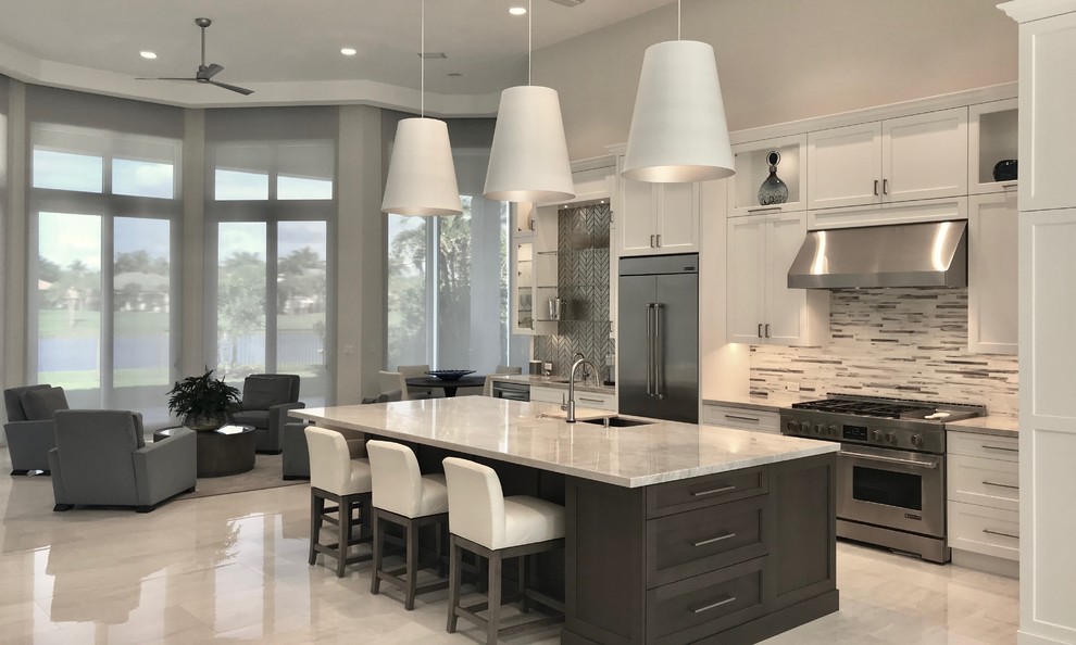 Photo of a large mediterranean galley open plan kitchen in Miami with an undermount sink, shaker cabinets, white cabinets, quartzite benchtops, multi-coloured splashback, glass tile splashback, stainless steel appliances, porcelain floors, with island, white floor and beige benchtop.