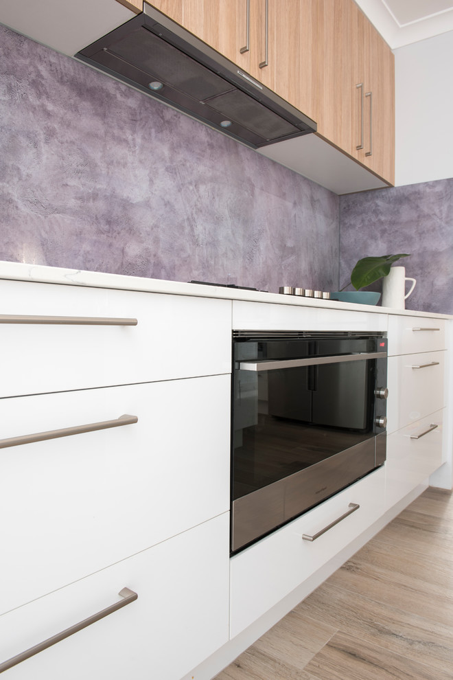 This is an example of a mid-sized modern open plan kitchen in Perth with an undermount sink, quartz benchtops, glass sheet splashback, stainless steel appliances and light hardwood floors.