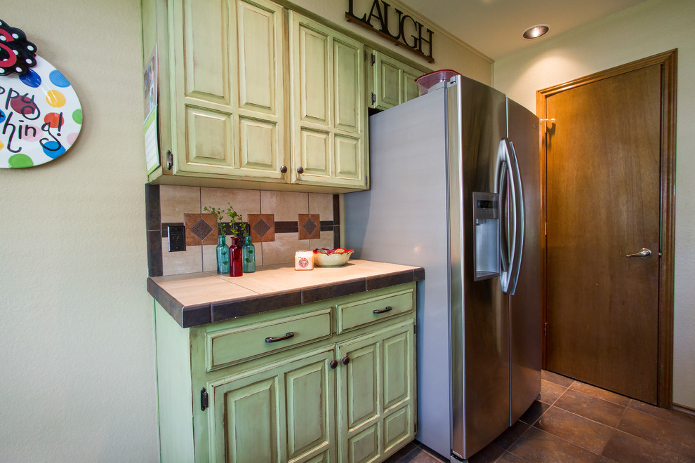 Mid-sized traditional l-shaped eat-in kitchen in Austin with raised-panel cabinets, green cabinets, tile benchtops, beige splashback, ceramic splashback, stainless steel appliances and ceramic floors.