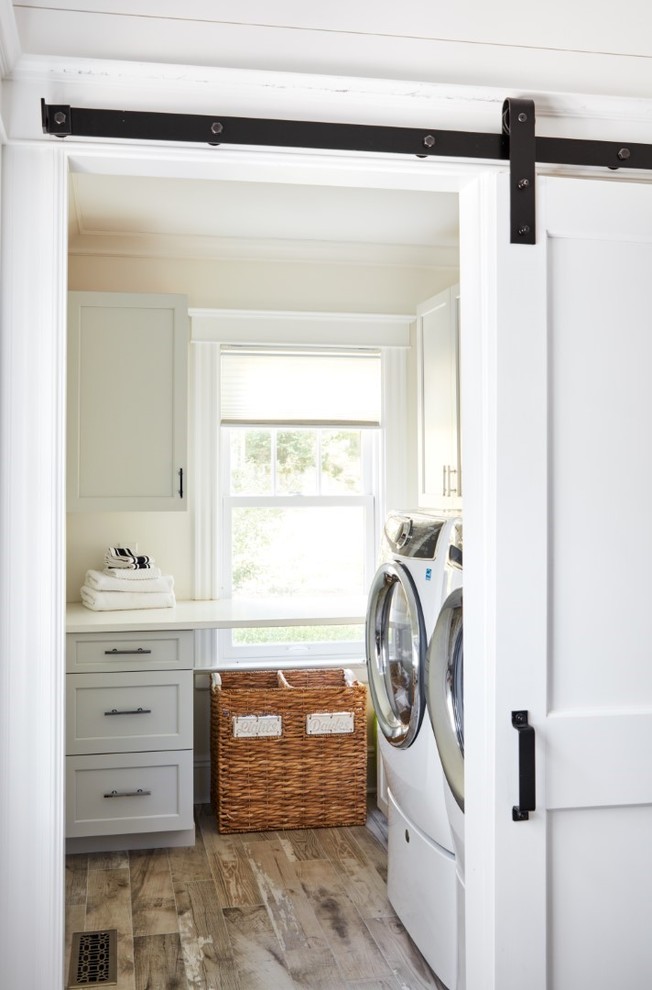 This is an example of a mid-sized industrial l-shaped dedicated laundry room in New York with an undermount sink, recessed-panel cabinets, grey cabinets, quartz benchtops, beige walls, porcelain floors, a side-by-side washer and dryer, multi-coloured floor and white benchtop.