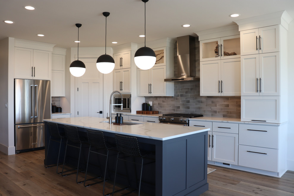 Open concept kitchen - large transitional l-shaped medium tone wood floor and brown floor open concept kitchen idea with a single-bowl sink, shaker cabinets, white cabinets, quartz countertops, gray backsplash, subway tile backsplash, stainless steel appliances, an island and white countertops