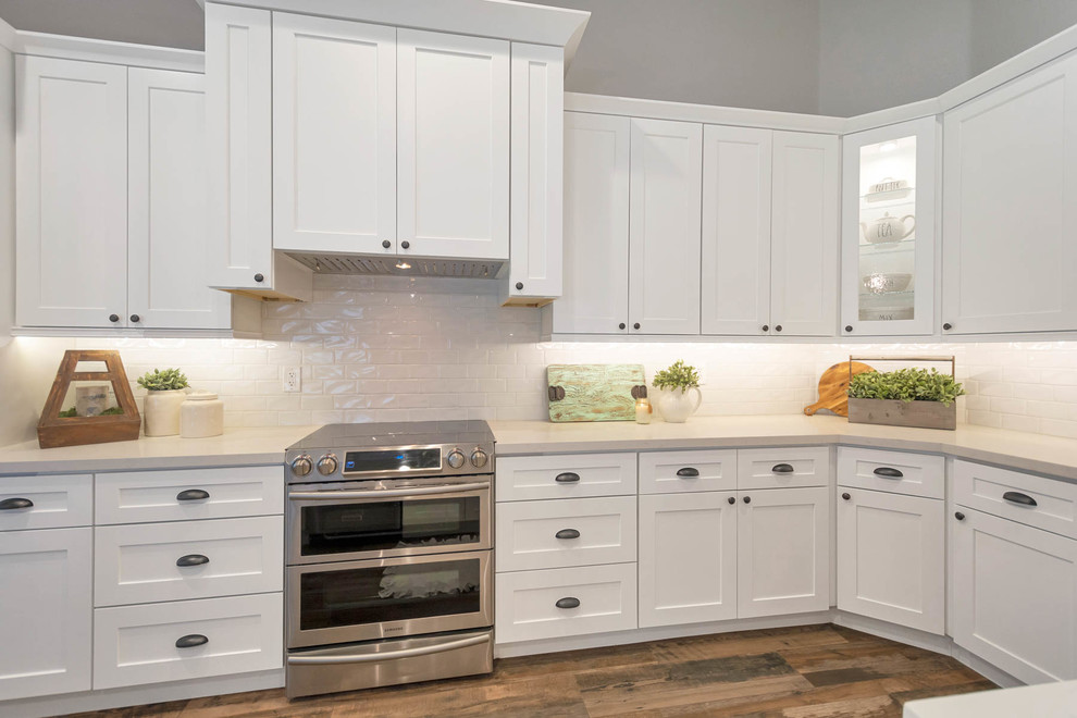 Photo of a large country l-shaped open plan kitchen in Phoenix with a farmhouse sink, shaker cabinets, white cabinets, quartz benchtops, white splashback, subway tile splashback, stainless steel appliances, with island and white benchtop.