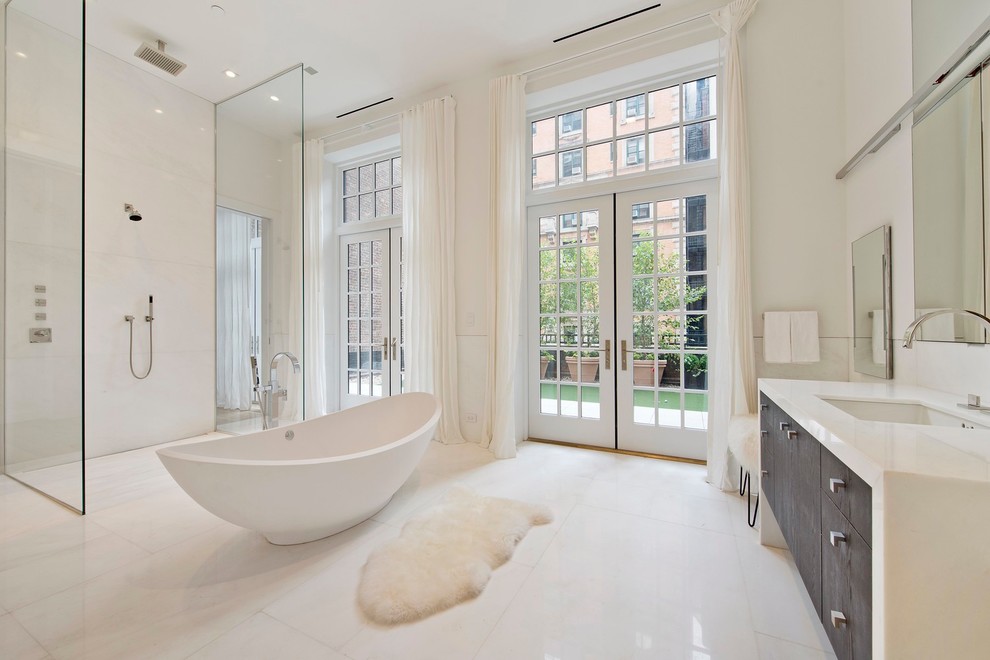 This is an example of a modern bathroom in New York with an undermount sink, dark wood cabinets, marble benchtops, a freestanding tub, an open shower, white tile, stone slab, white walls, marble floors, white floor and white benchtops.