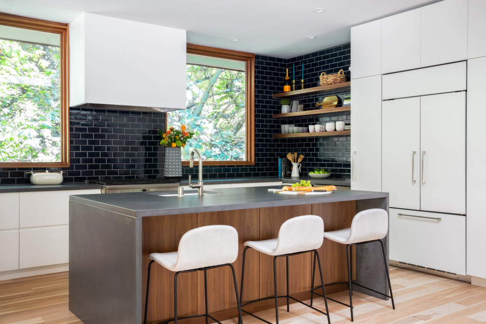 This is an example of a midcentury l-shaped kitchen in San Francisco with an undermount sink, flat-panel cabinets, white cabinets, black splashback, subway tile splashback, stainless steel appliances, light hardwood floors, with island, beige floor and grey benchtop.