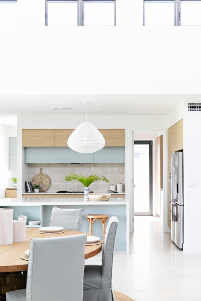 Design ideas for a mid-sized beach style galley open plan kitchen in Gold Coast - Tweed with an undermount sink, flat-panel cabinets, light wood cabinets, quartz benchtops, beige splashback, ceramic splashback, stainless steel appliances, ceramic floors, with island, white floor and white benchtop.