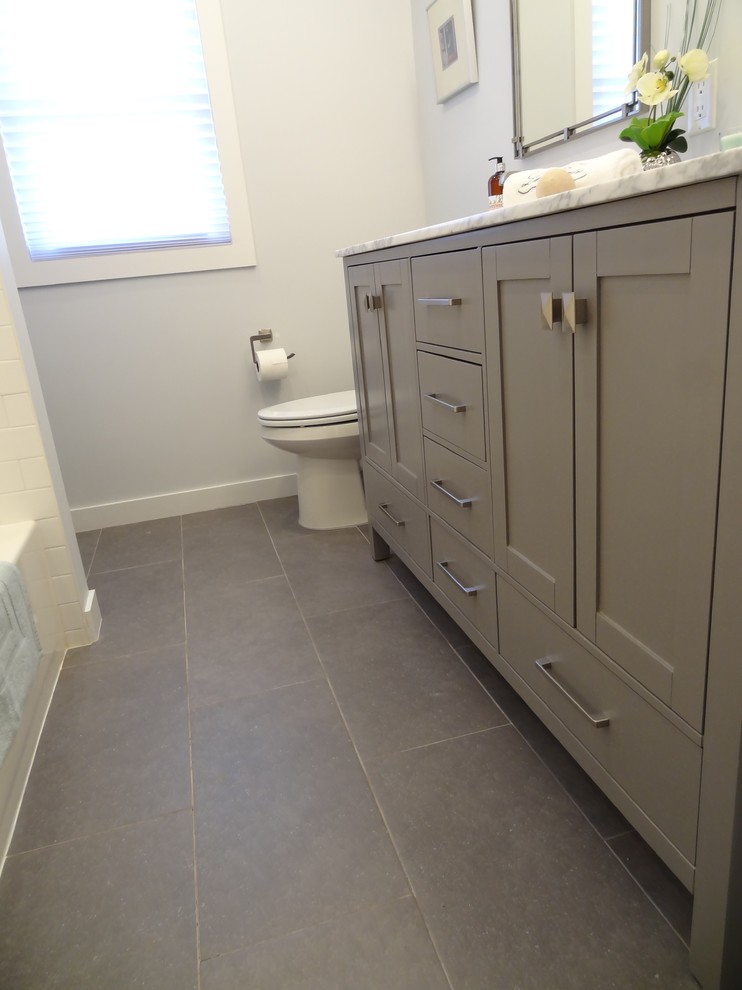 Inspiration for a small transitional kids bathroom in New York with shaker cabinets, grey cabinets, a shower/bathtub combo, a two-piece toilet, gray tile, ceramic tile, grey walls, porcelain floors, an undermount sink, marble benchtops, grey floor, a sliding shower screen and white benchtops.