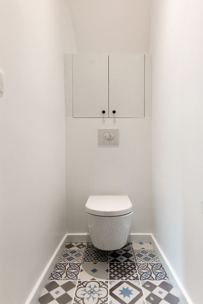 Design ideas for a small contemporary powder room in Paris with flat-panel cabinets, white cabinets, a wall-mount toilet, white walls, cement tiles and blue floor.