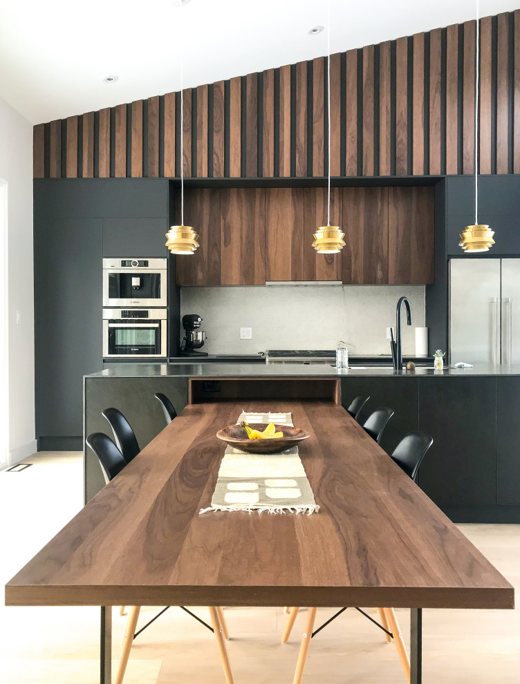 Design ideas for a mid-sized midcentury galley open plan kitchen in Toronto with an undermount sink, flat-panel cabinets, black cabinets, tile benchtops, beige splashback, porcelain splashback, stainless steel appliances, light hardwood floors, with island and black benchtop.