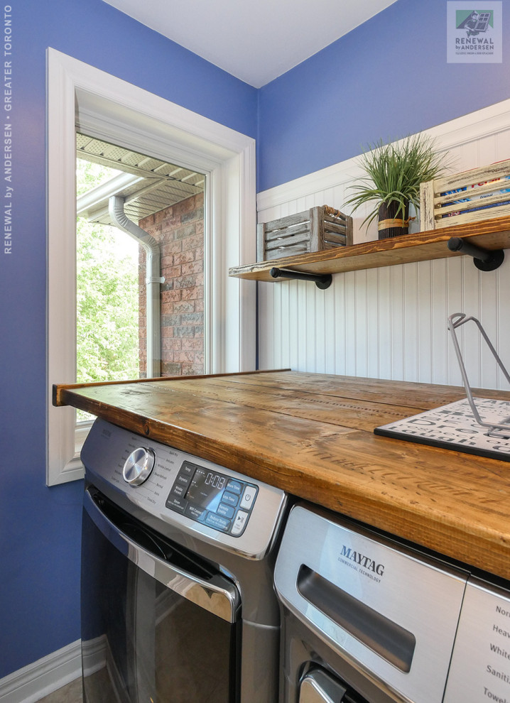 Foto på en mellanstor linjär tvättstuga enbart för tvätt, med träbänkskiva, blå väggar, klinkergolv i keramik, en tvättmaskin och torktumlare bredvid varandra och beiget golv