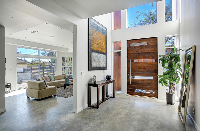 Inspiration for a mid-sized modern front door in Los Angeles with white walls, concrete floors, a pivot front door and a dark wood front door.