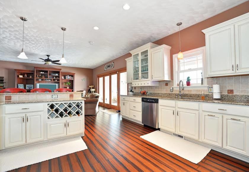 Transitional bamboo floor eat-in kitchen photo with raised-panel cabinets, white cabinets, granite countertops, beige backsplash, ceramic backsplash and stainless steel appliances