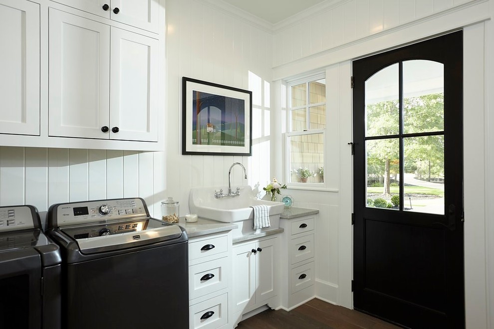 Inspiration for a mid-sized traditional single-wall dedicated laundry room in Austin with a farmhouse sink, shaker cabinets, white cabinets, granite benchtops, white walls, dark hardwood floors, a side-by-side washer and dryer and brown floor.