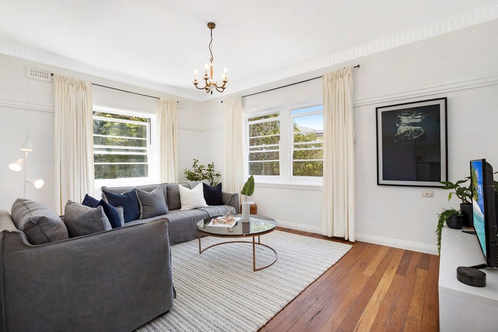 Photo of a large traditional enclosed living room in Sydney with white walls, medium hardwood floors, a freestanding tv and brown floor.