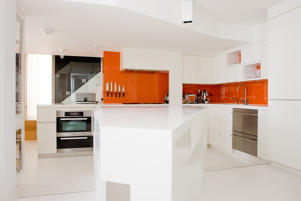 Design ideas for a mid-sized contemporary l-shaped eat-in kitchen in London with an undermount sink, flat-panel cabinets, white cabinets, orange splashback, glass sheet splashback, stainless steel appliances, with island and solid surface benchtops.