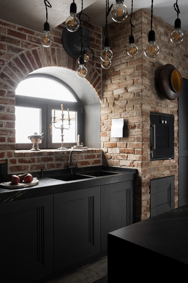 Bild på ett mellanstort funkis svart svart kök, med en dubbel diskho, marmorbänkskiva, rött stänkskydd, stänkskydd i tegel, svarta vitvaror, en köksö och grått golv