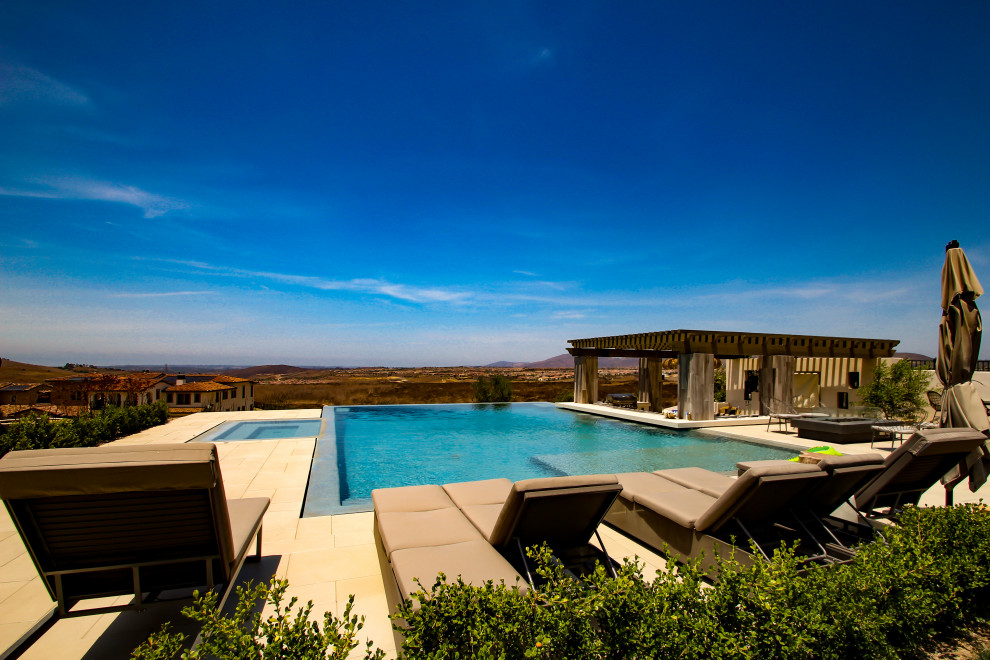 Ejemplo de piscina infinita contemporánea grande rectangular en patio trasero con paisajismo de piscina y suelo de baldosas