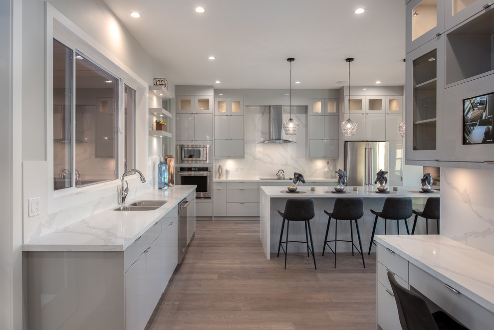 Inspiration for a modern u-shaped kitchen in Vancouver with an undermount sink, flat-panel cabinets, grey cabinets, marble benchtops, white splashback, marble splashback, stainless steel appliances, medium hardwood floors, with island, brown floor and white benchtop.